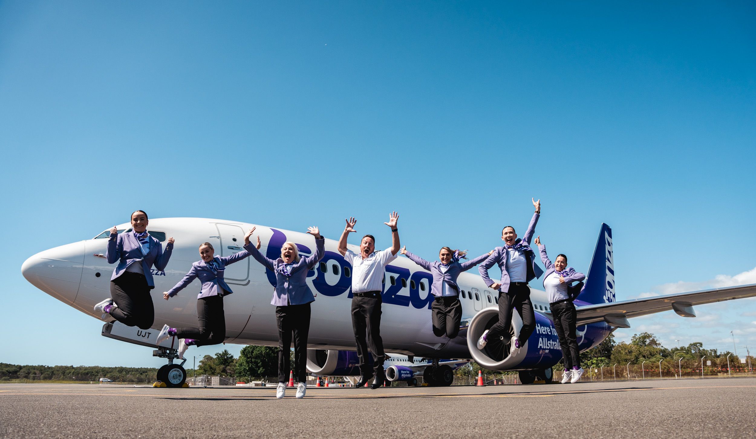 Bonza flight attendants jumping with excitement in front of a Bonza airplane.